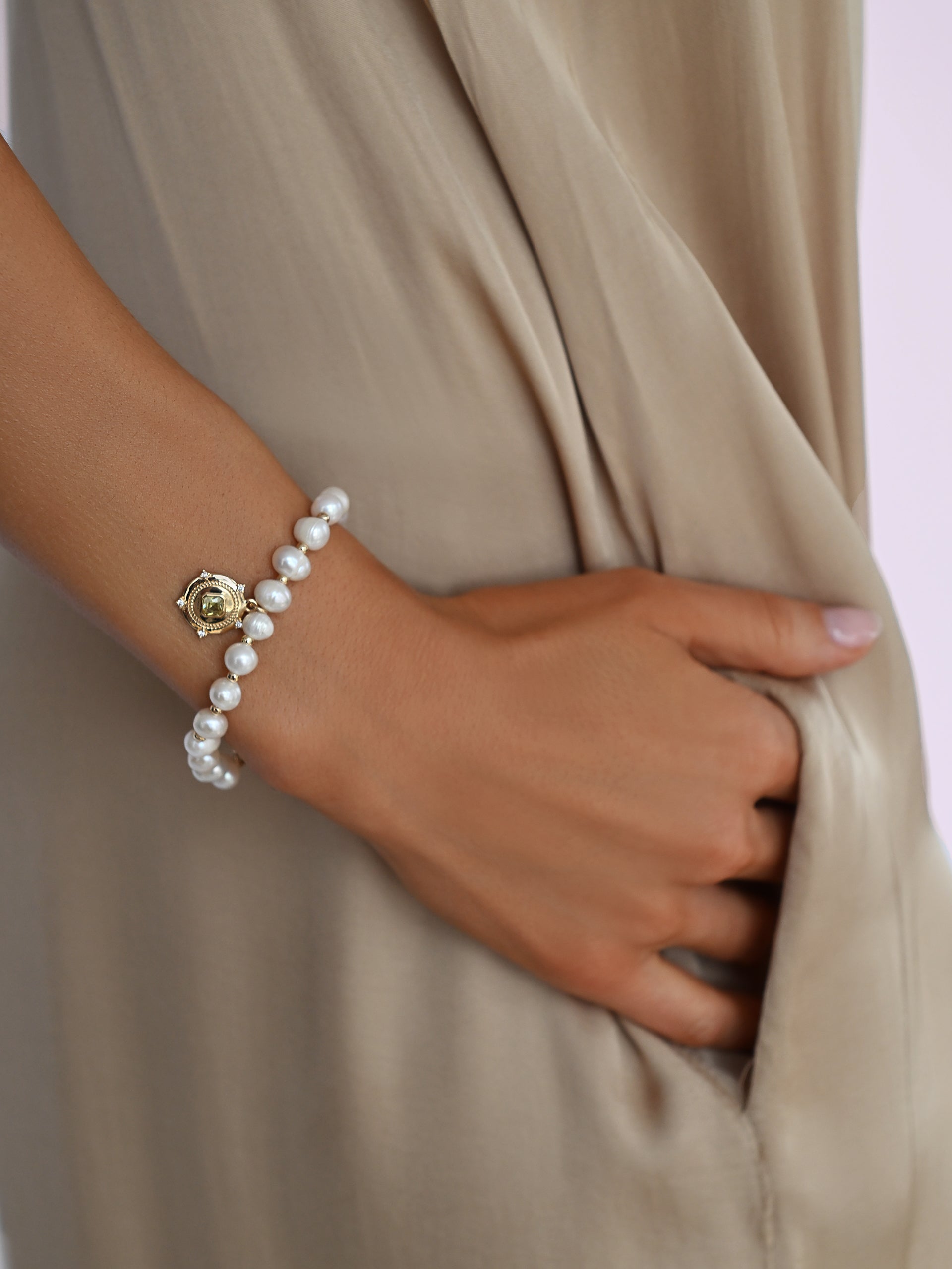 Penelope freshwater pearl bracelet with gold spacers and pale green cubic zirconia charm worn on the wrist with a neutral satin dress.