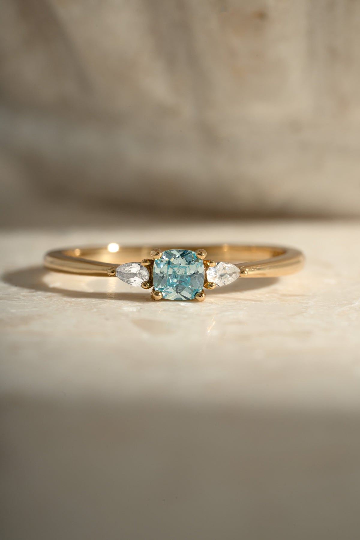 Close-up of gold Kennedy Cushion Ring with blue cushion-cut cubic zirconia and clear side stones