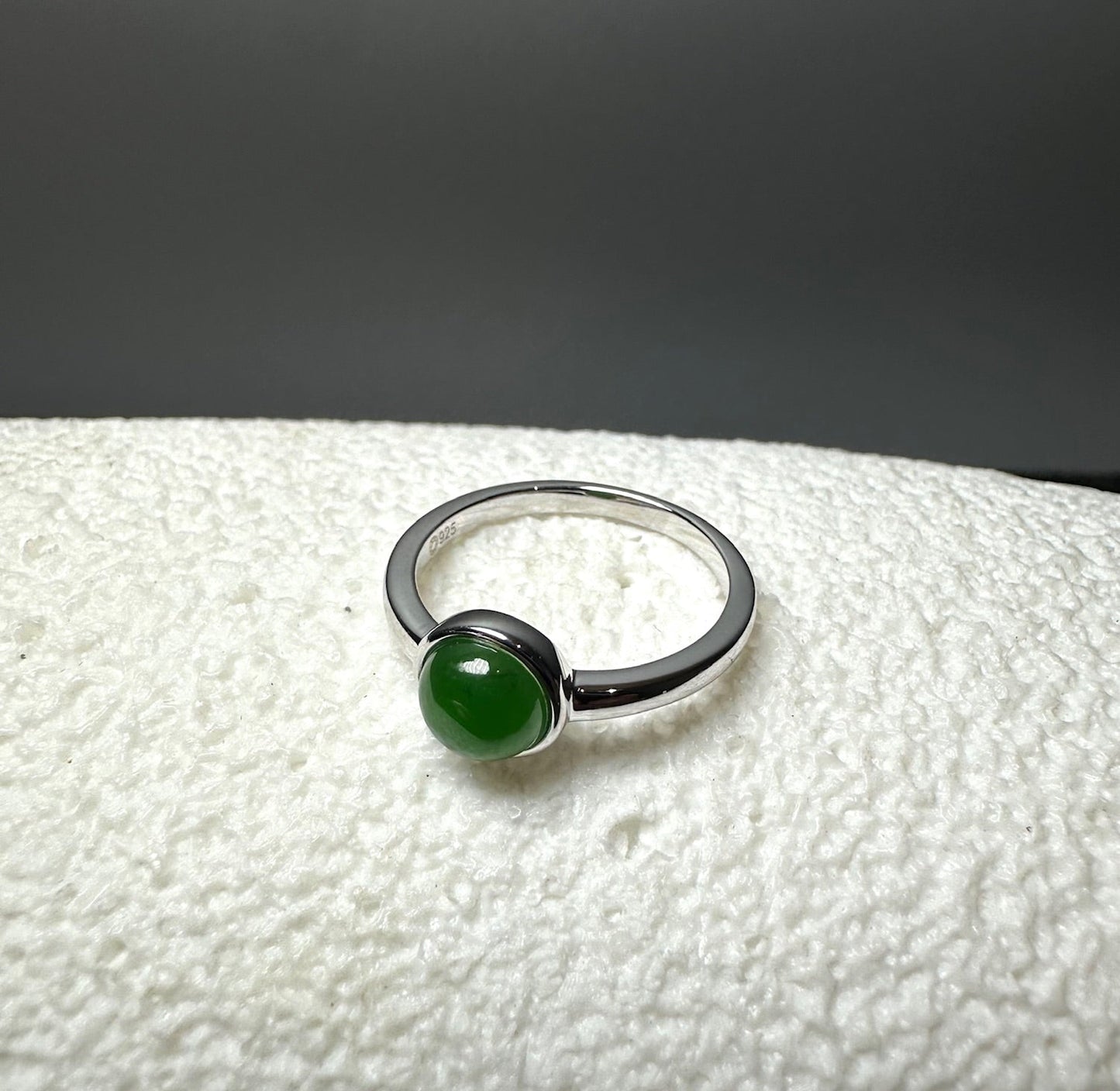     Blaise sterling silver ring with a round green nephrite jade cabochon shown at an angle on a textured white surface.