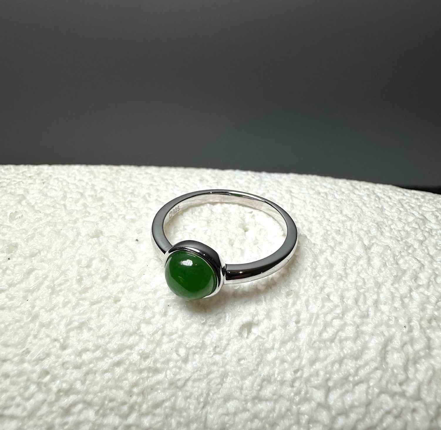     Blaise sterling silver ring with a round green nephrite jade cabochon shown at an angle on a textured white surface.