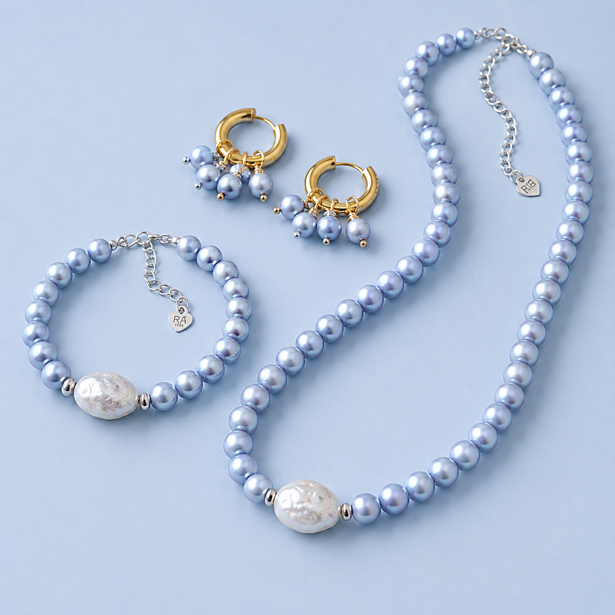 Blu Pearl Collection with light blue pearl necklace, matching bracelet, gold hoop earrings and coordinating pearl jewelry on a light blue background.