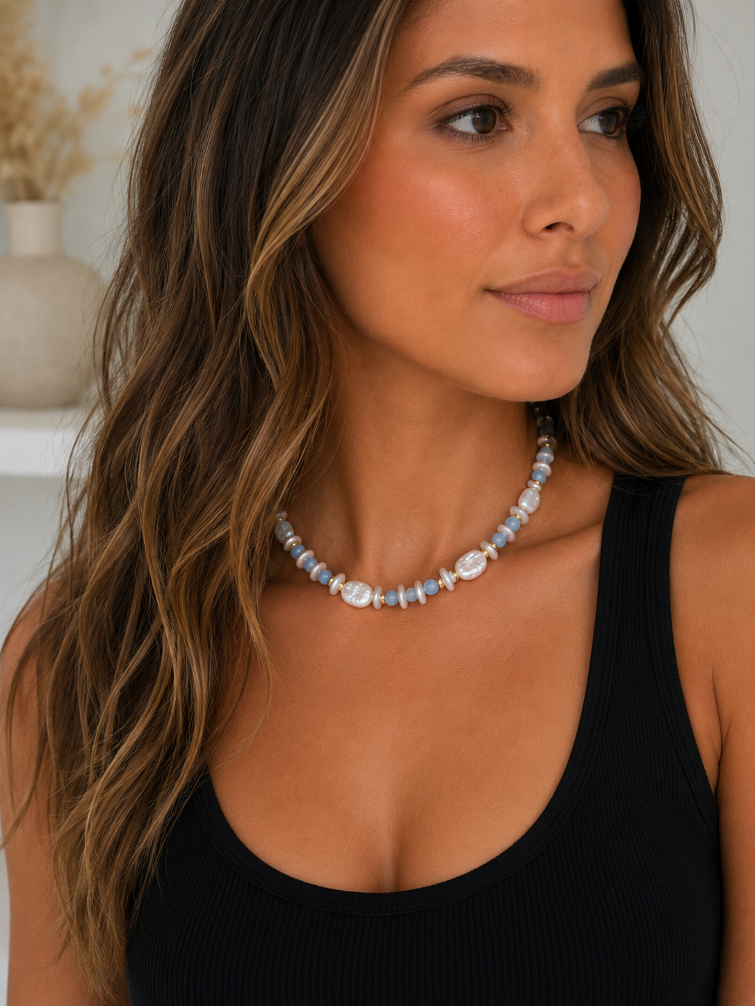 White pearl and light blue beaded necklace worn with a black ribbed tank top