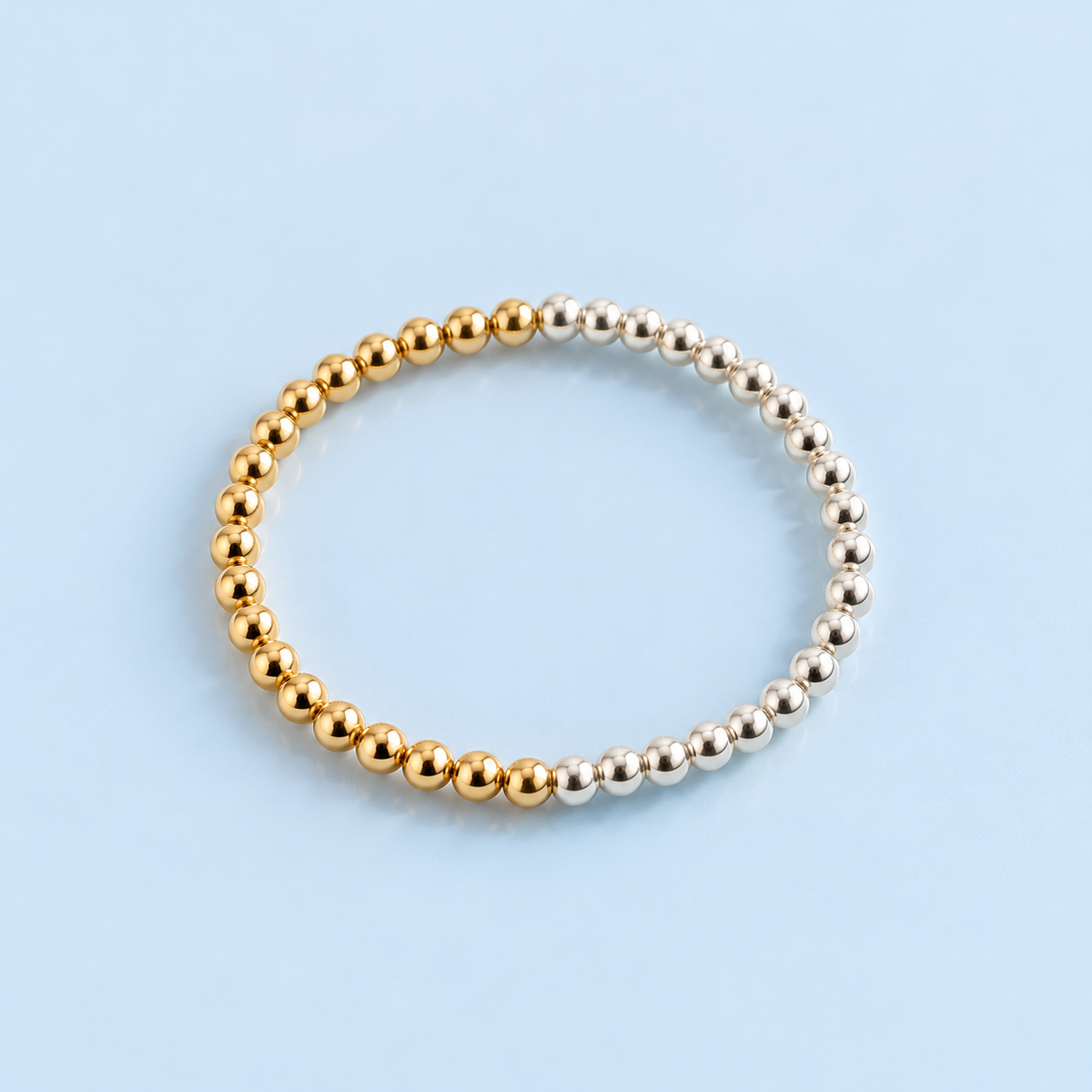 Brighton sterling silver and 14K gold-filled 5 mm beaded bracelet from The Riann Ashlyn Collection, featuring two contrasting sections of gold and silver beads on a pale blue background.