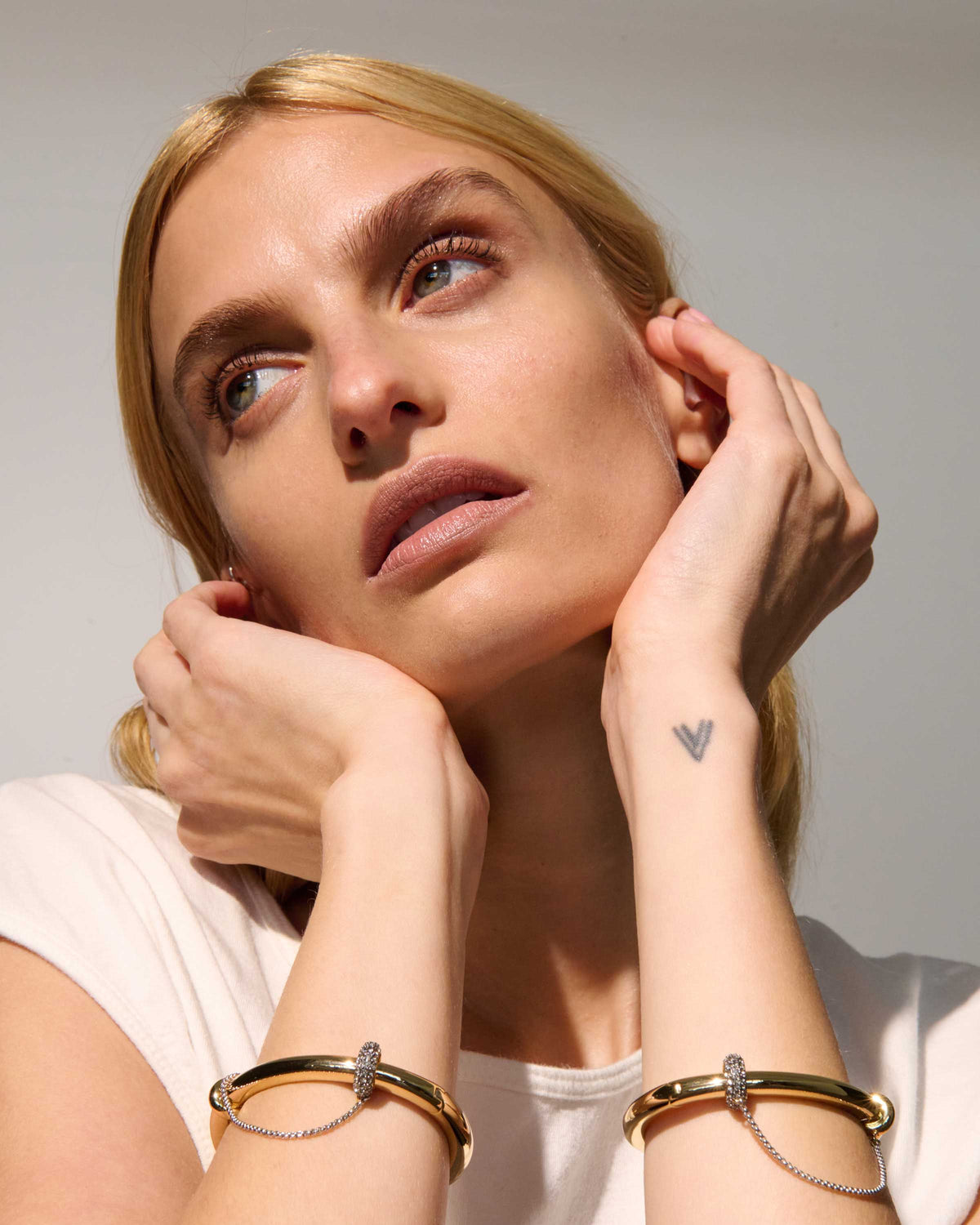 Channing Sculptural Bangle Bracelet from The Riann Ashlyn Collection, worn by a model in an editorial jewelry photograph with her hands near her face.
