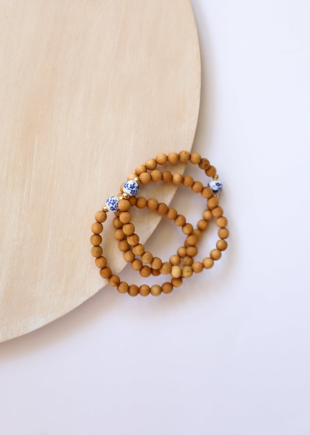 Cypress natural wood bead bracelets with blue floral porcelain details displayed beside a pale wooden prop, The Riann Ashlyn Collection