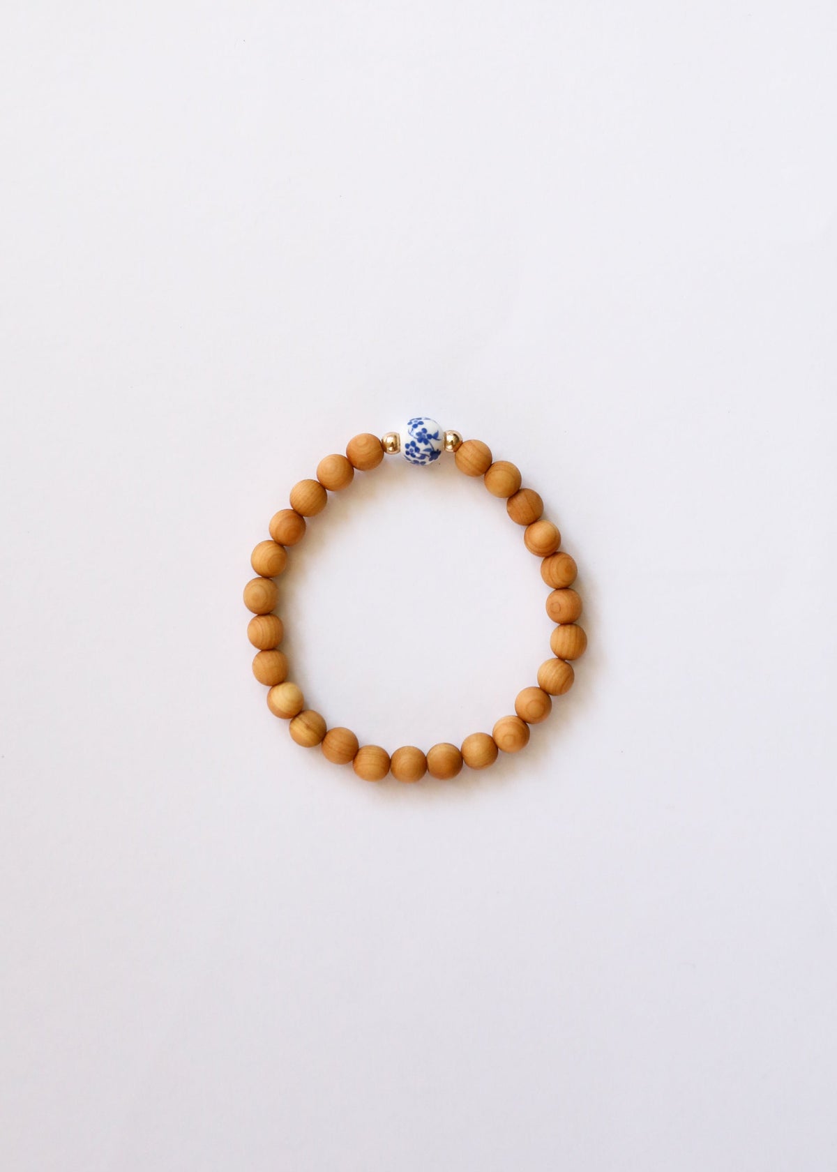 Three Cypress wood bracelets displayed in a hand with blue floral porcelain beads and gold-filled accents, The Riann Ashlyn Collection