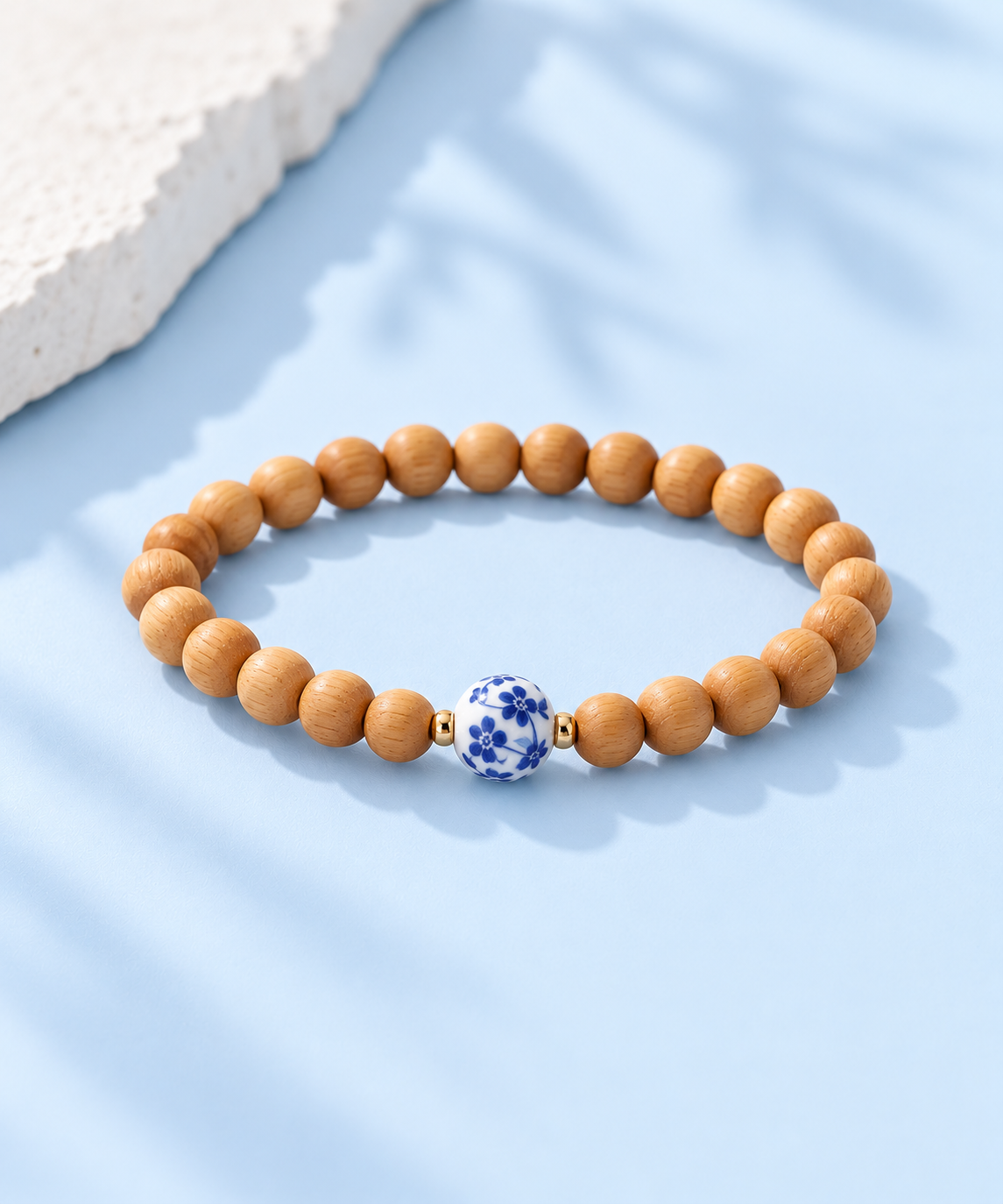 Cypress wood bead bracelet with blue-and-white floral porcelain bead and 14K gold-filled accents on pale blue background, The Riann Ashlyn Collection.