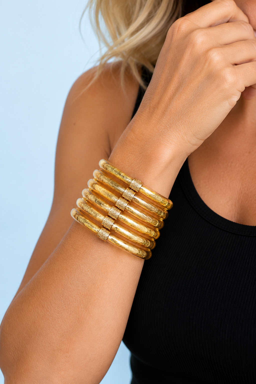 Model wearing six Demi Gold All Weather Bangles together on her wrist with a black sleeveless top — The Riann Ashlyn Collection