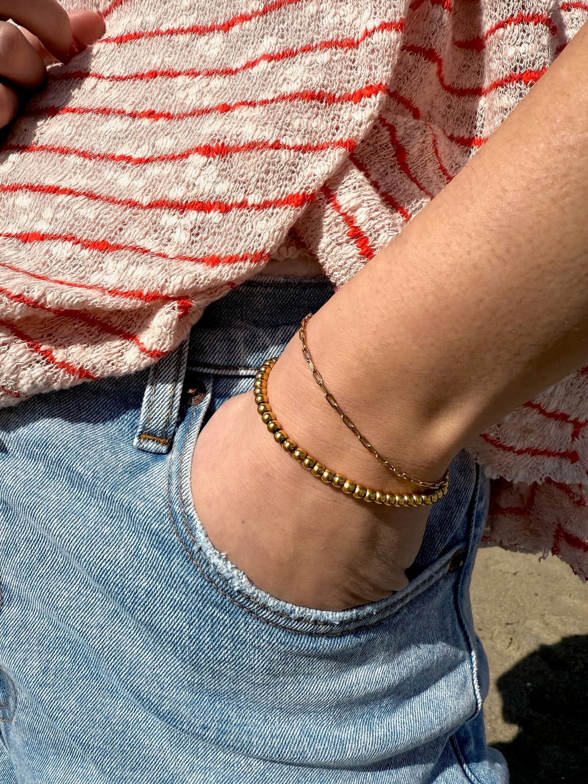 Ellie gold beaded bracelet layered with a delicate chain bracelet and denim outfit
