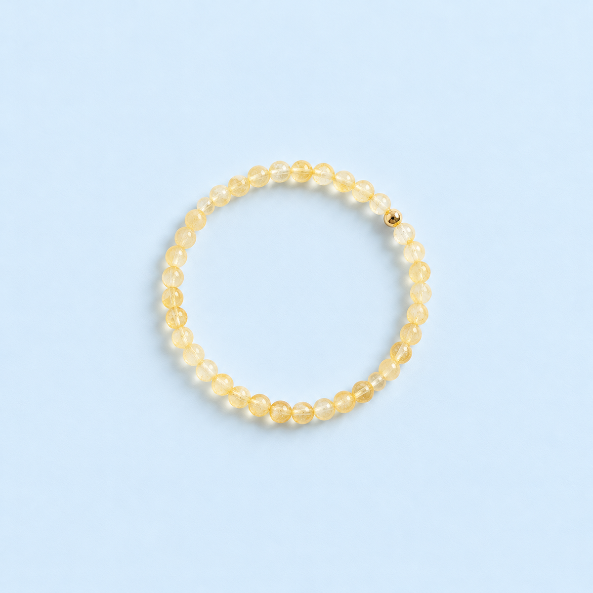 Fia Citrine & 14K Gold-Filled Beaded Stretch Bracelet from The Riann Ashlyn Collection, featuring delicate pale yellow citrine beads and a single polished gold-filled accent bead on a pale blue background.