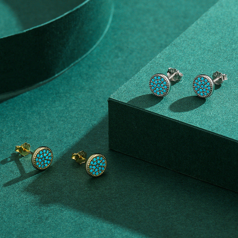    Gemma turquoise stud earrings in silver and gold displayed on a teal surface