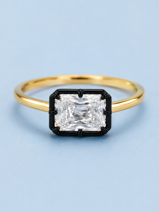 Georgia radiant-cut cubic zirconia ring with black-tone setting and gold band on a light blue background
