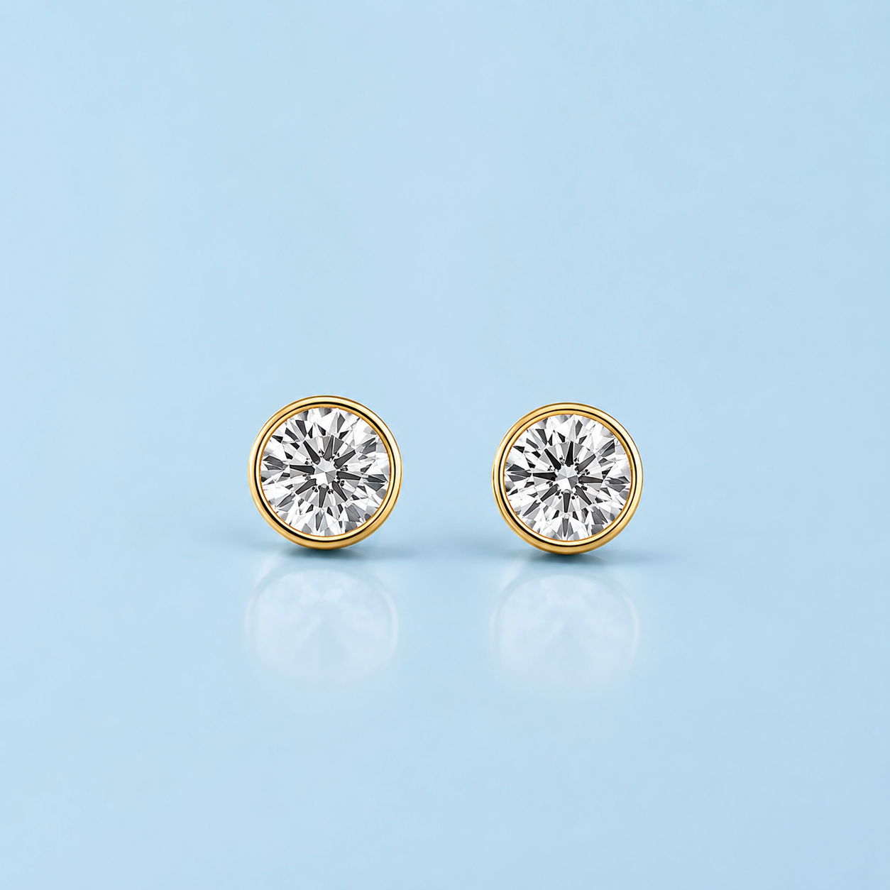 Gold bezel-set stud earrings with round clear stones on a light blue background