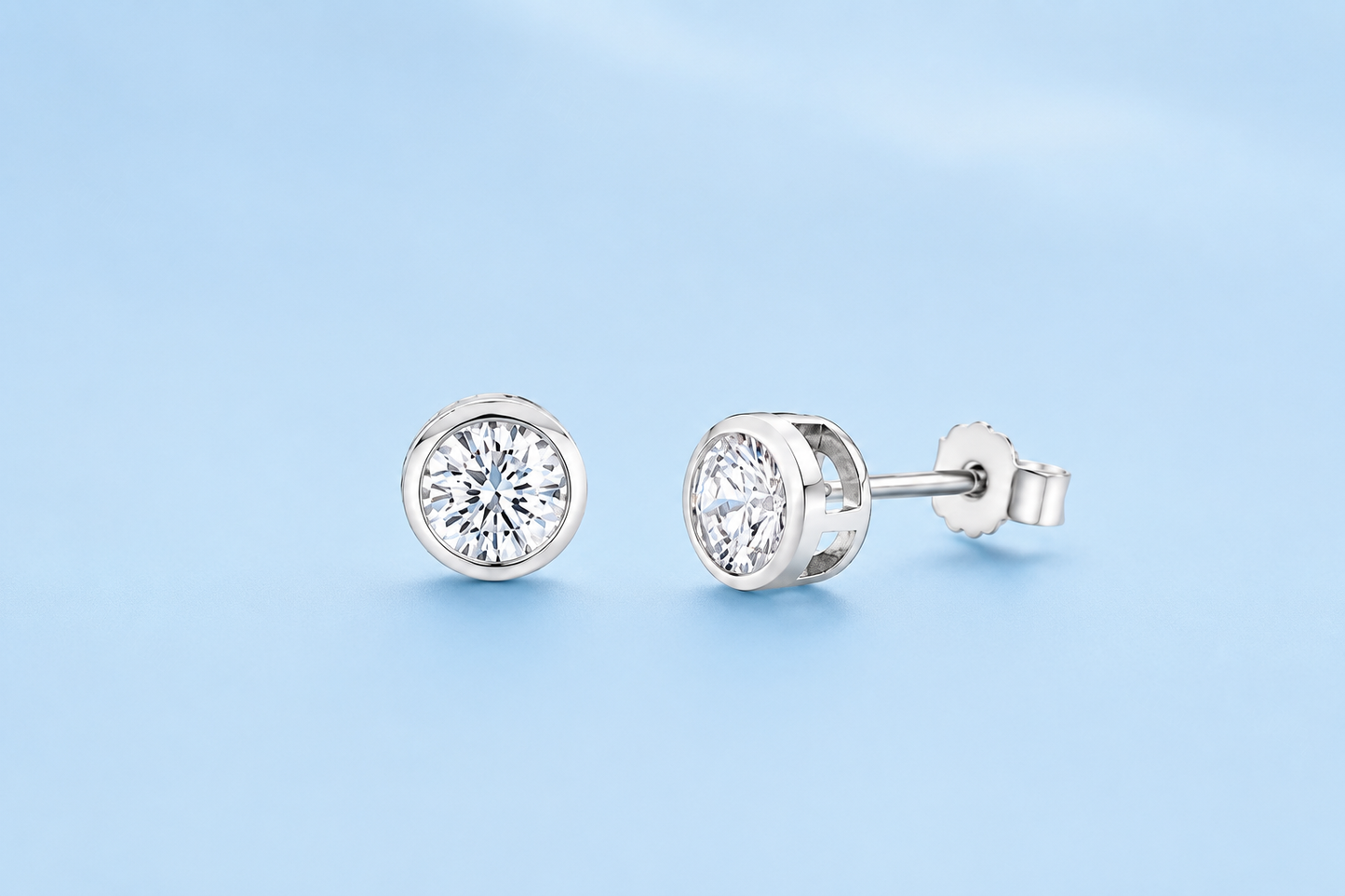Harper sterling silver simulated diamond bezel-set stud earrings on a light blue background, shown from front and side.