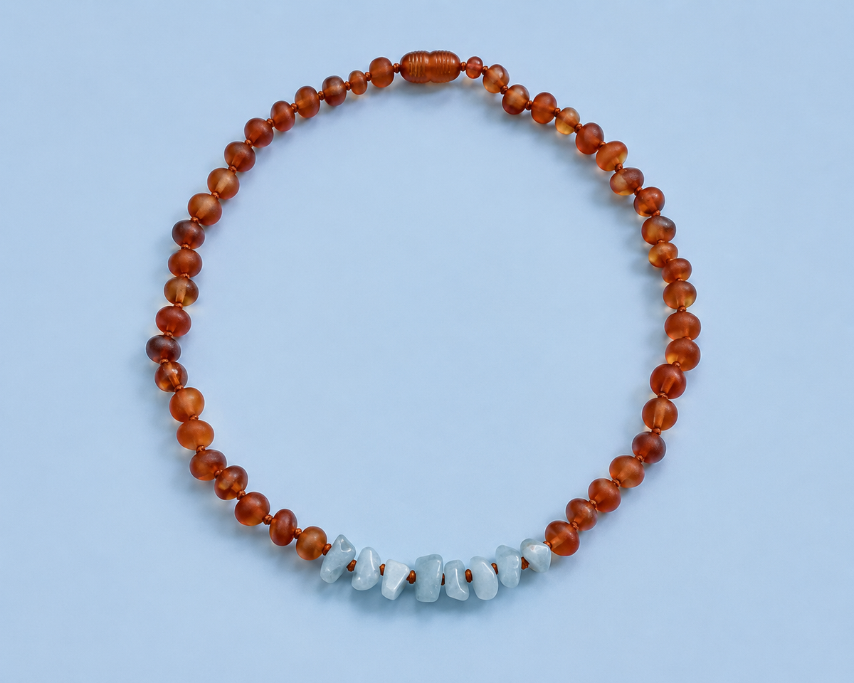 Hollis Necklace featuring warm cognac Baltic amber beads and a center of pale blue raw aquamarine chips on a light blue background.