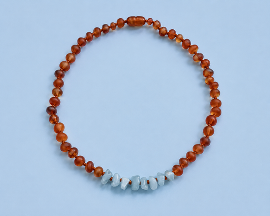 Hollis Necklace featuring warm cognac Baltic amber beads and a center of pale blue raw aquamarine chips on a light blue background.