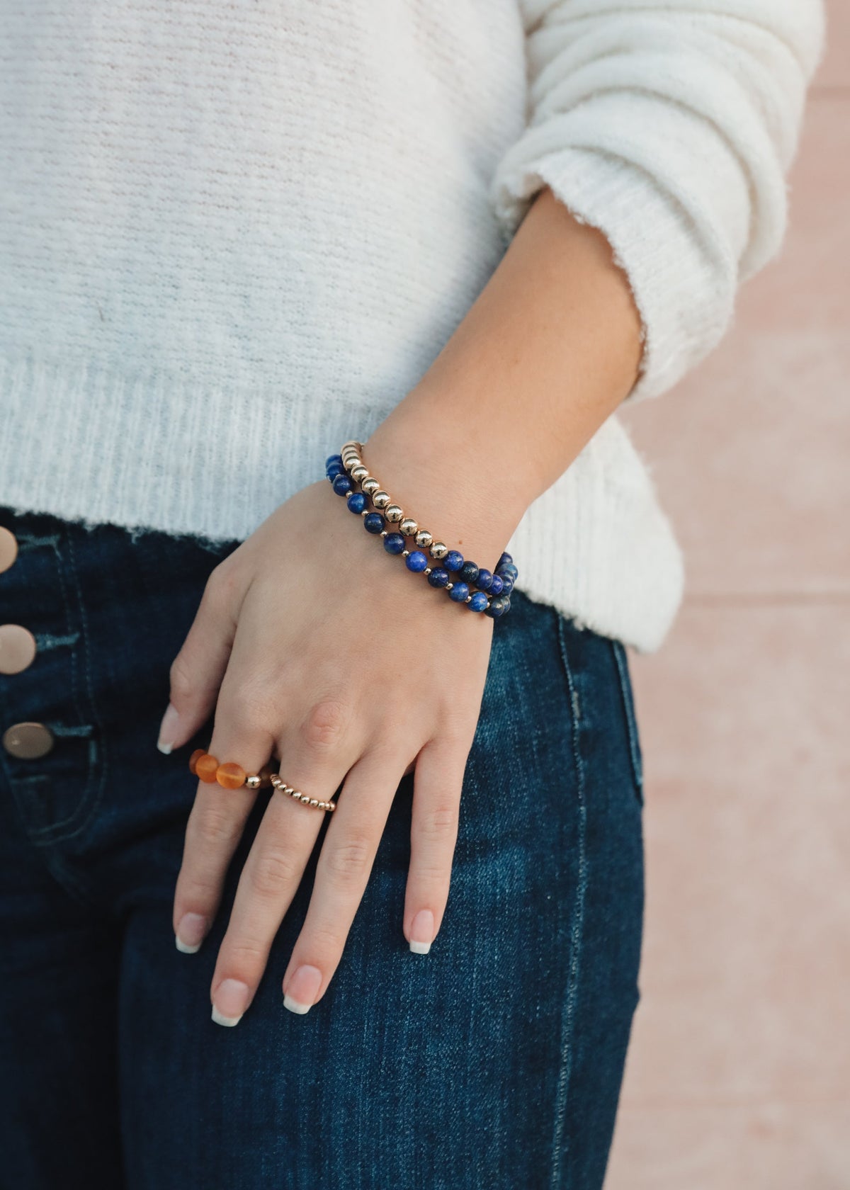 Model wearing an individual Indi blue lapis lazuli bracelet from The Riann Ashlyn Collection with a light sweater and dark denim.