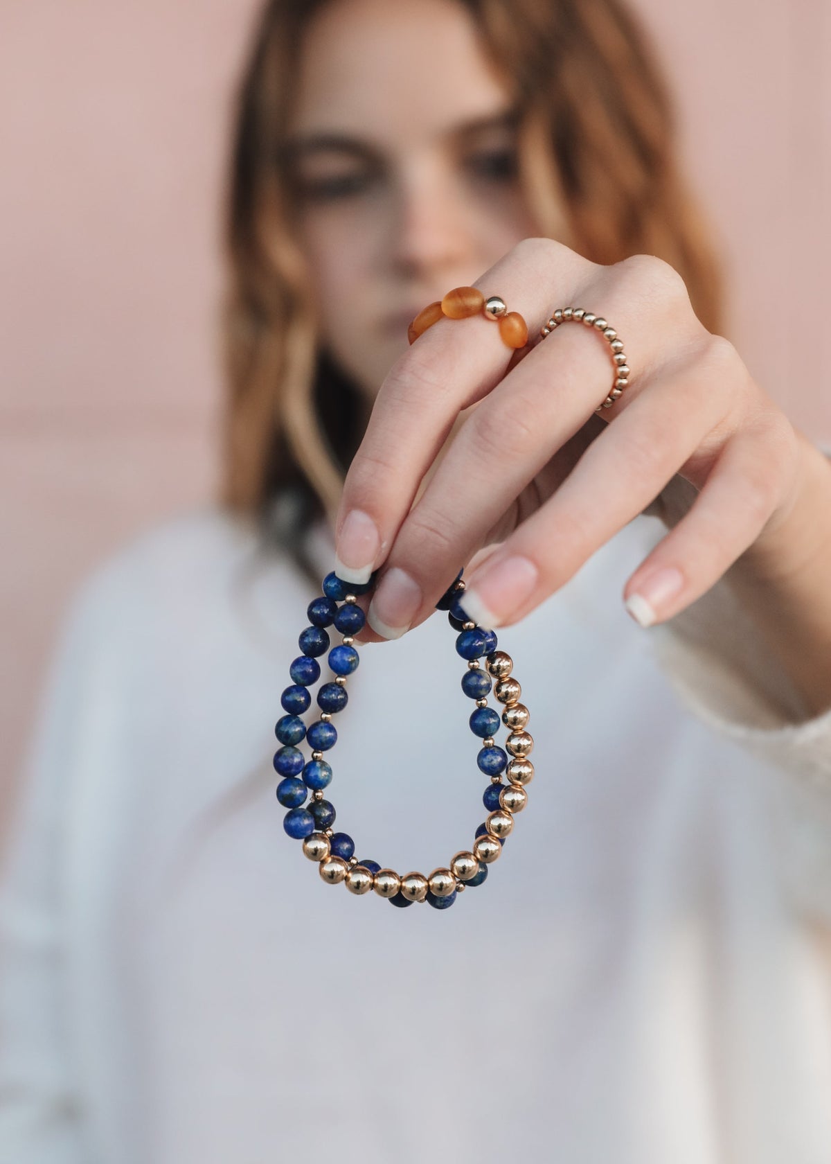 Model holding an Indi lapis lazuli and 14K gold-filled beaded stretch bracelet from The Riann Ashlyn Collection, showing its contrasting blue and gold beads.