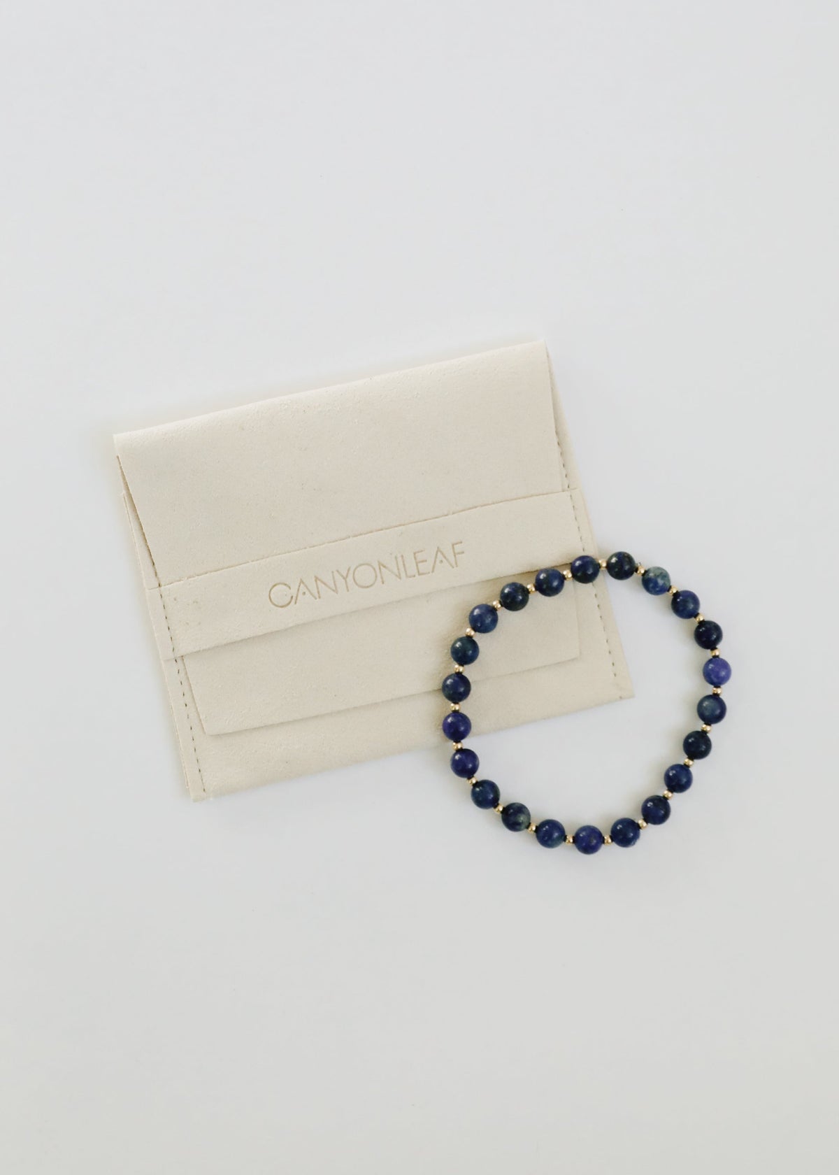 Individual Indi lapis lazuli stretch bracelet from The Riann Ashlyn Collection, featuring blue gemstone beads with small 14K gold-filled spacers beside a jewelry pouch.