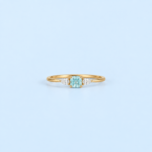 Gold Kennedy Aquamarine Blue Cushion Ring with blue cushion-cut cubic zirconia on Riann Ashlyn blue background