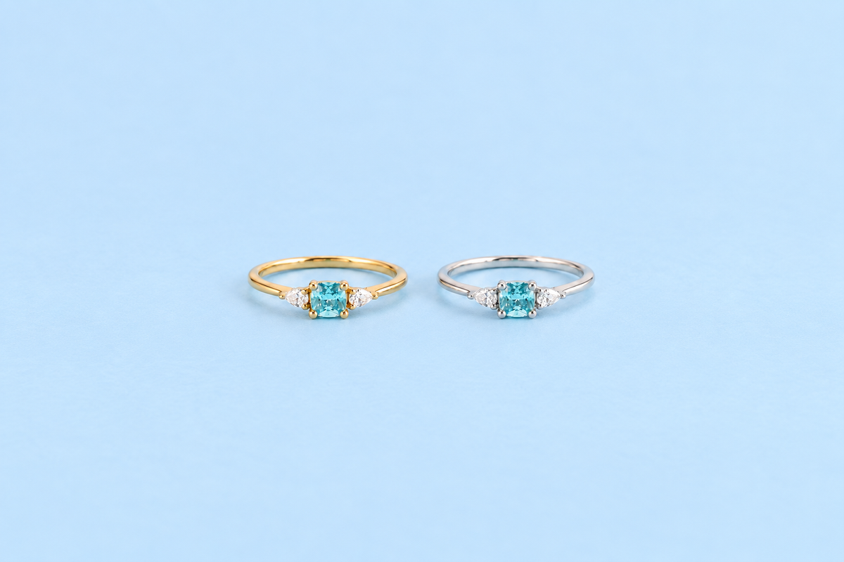 Gold and silver Kennedy Aquamarine Blue Cushion Rings with blue cushion-cut cubic zirconia on Riann Ashlyn blue background