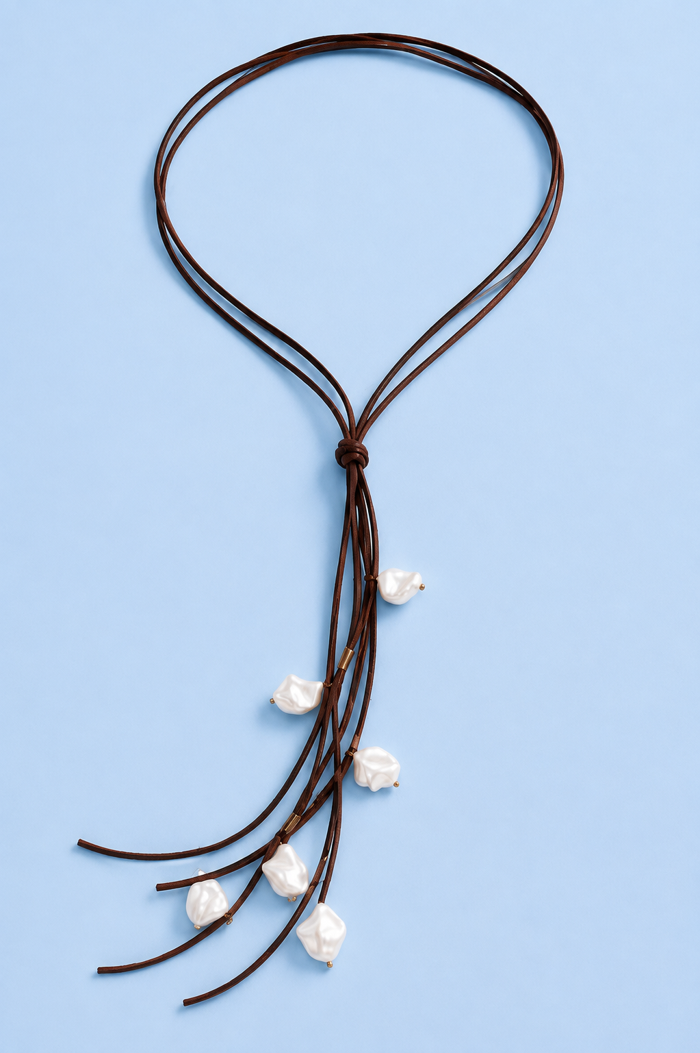 Close-up of the Koa long vegan leather pearl necklace with dark brown cords and irregular white shell pearl accents on a pale blue background