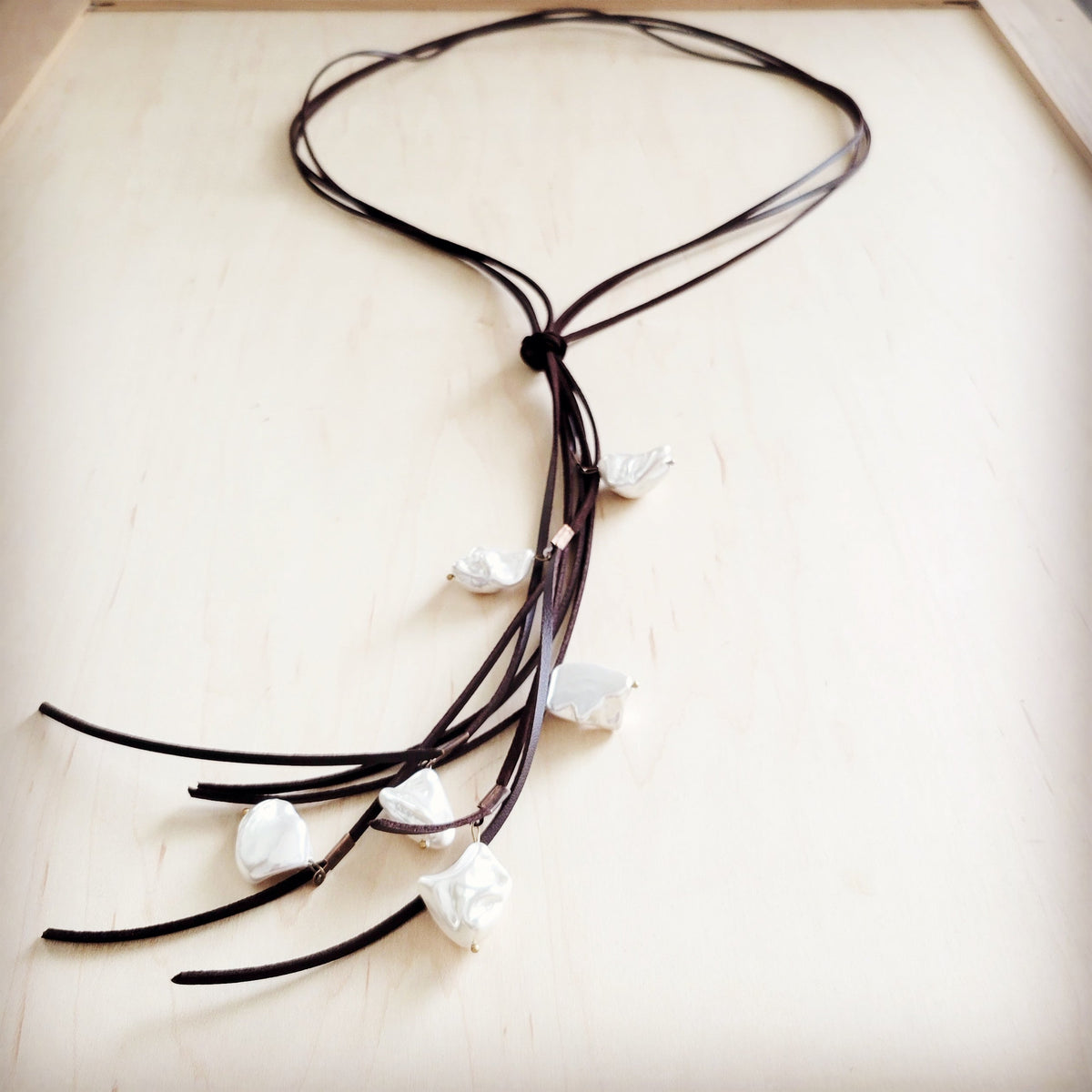 Close-up of the Koa long vegan leather pearl necklace showing dark brown cords, center knot, and irregular white shell pearl accents