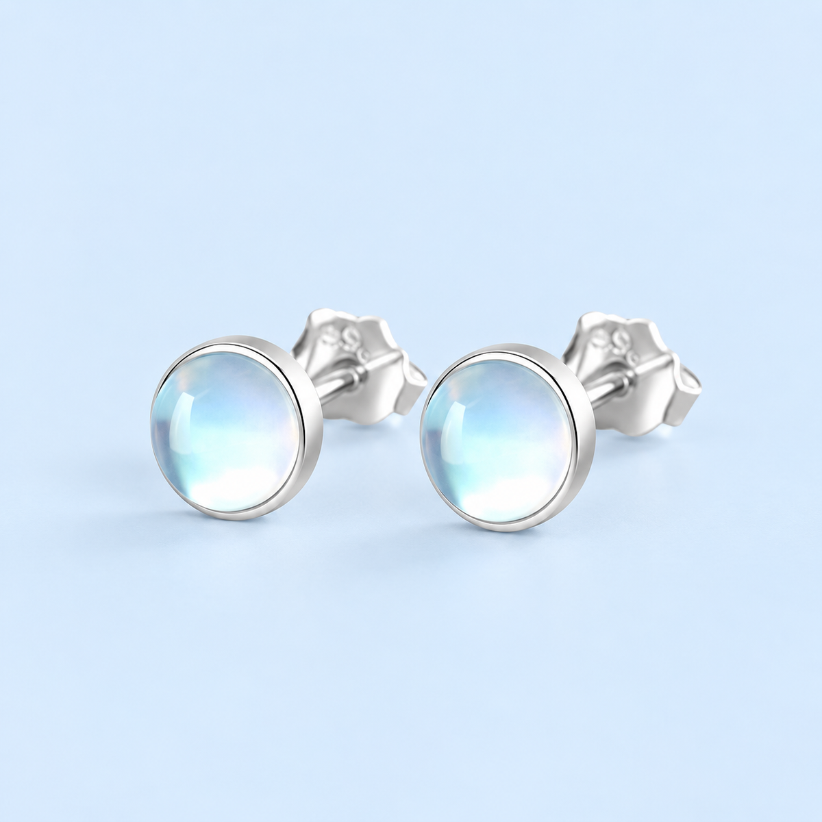 Lumi round moonstone stud earrings with sterling silver bezel settings and butterfly backs on a pale blue background.