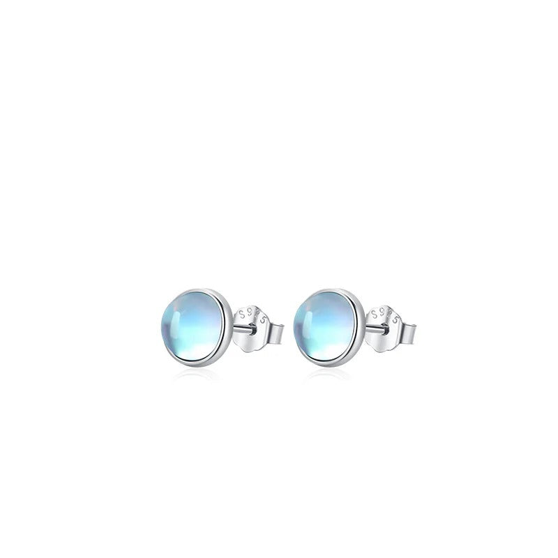 Large pair of Lumi round pale blue stud earrings with silver-tone settings on white.
