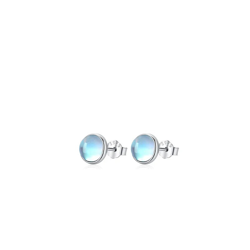 Medium pair of Lumi round pale blue stud earrings with silver-tone settings on white.
