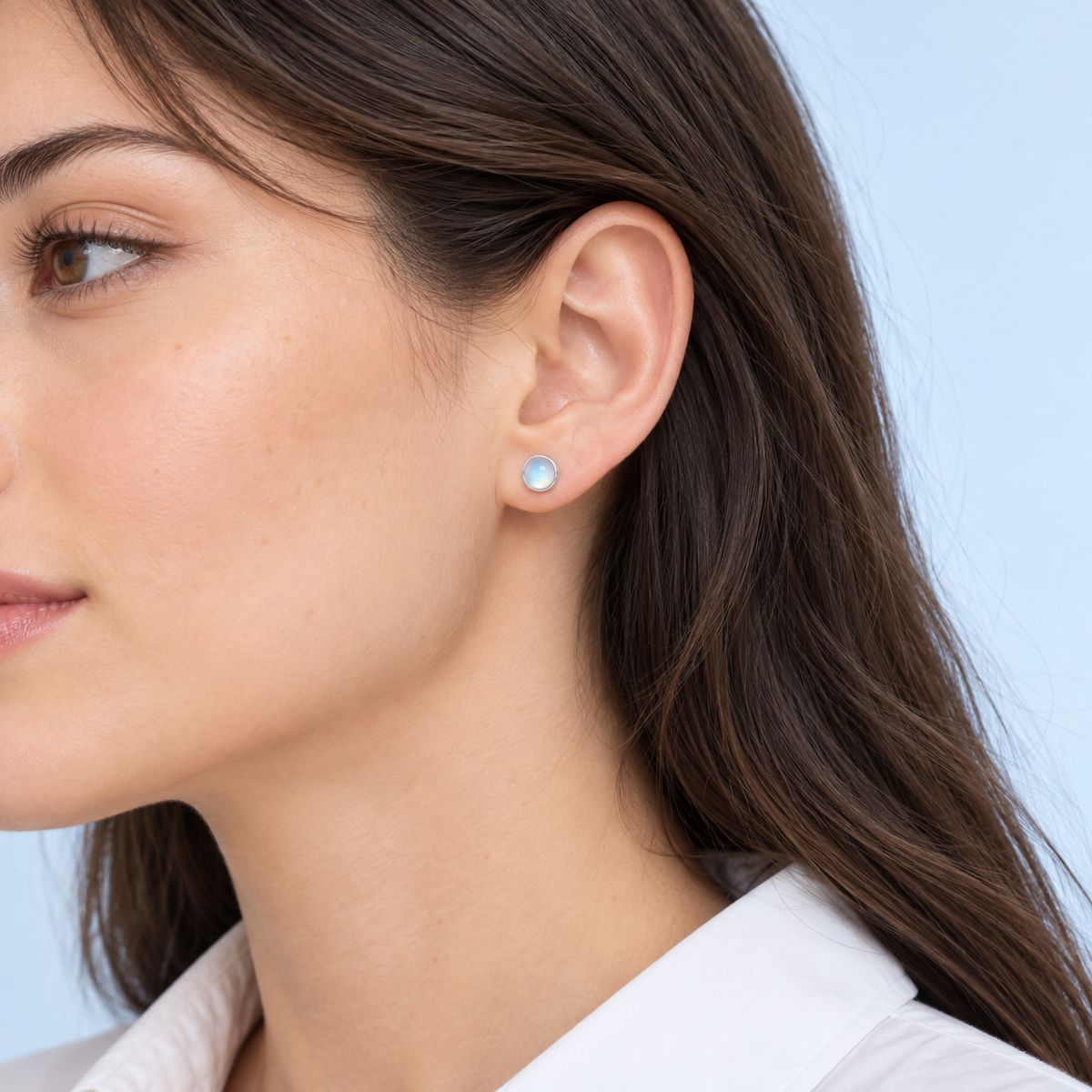 Close-up of a dark-haired model wearing a Lumi pale blue stud earring with a silver-tone bezel.