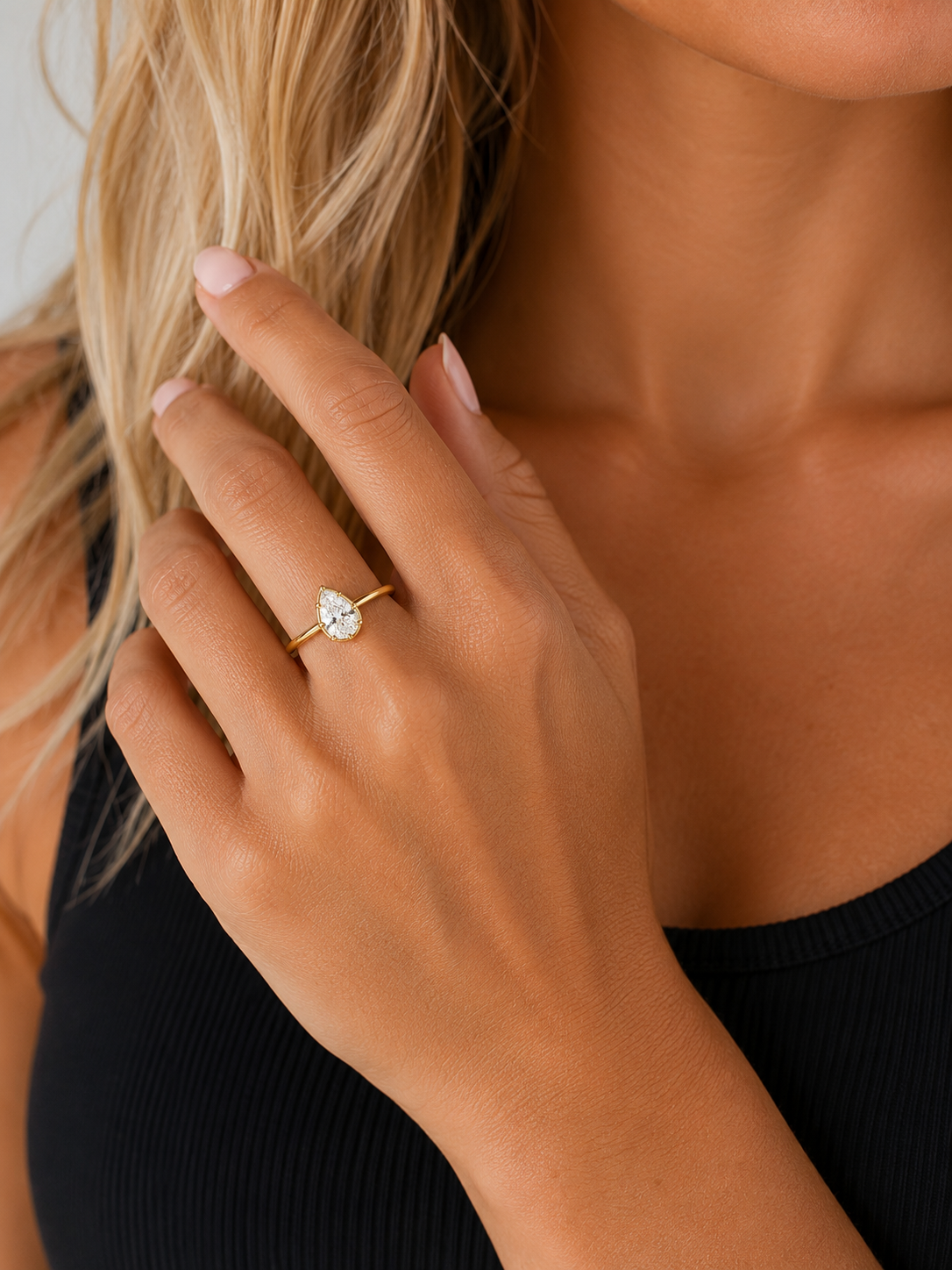 Woman wearing the Lux gold-tone pear-cut bezel ring with a clear center stone and black tank top