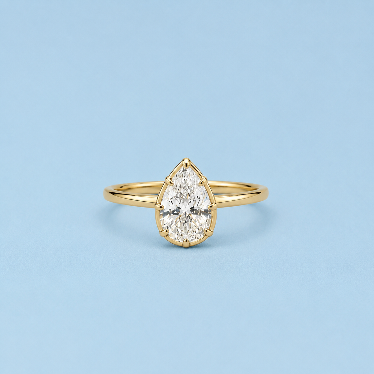 Lux pear-cut bezel ring in gold tone with a clear center stone on a light blue background
