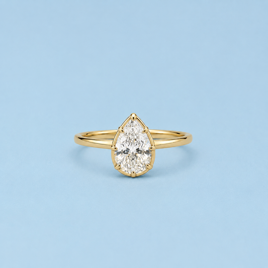 Lux pear-cut bezel ring in gold tone with a clear center stone on a light blue background