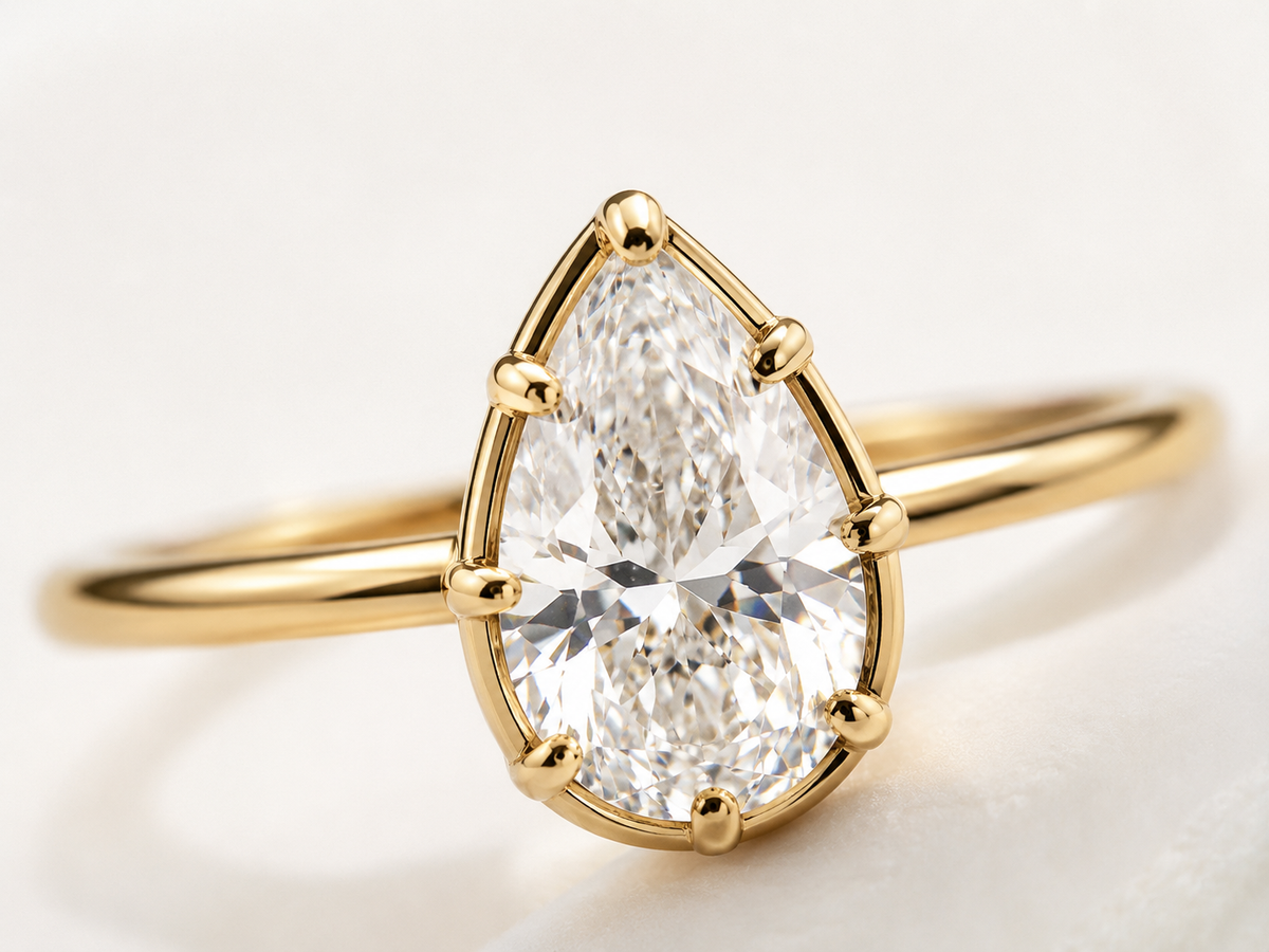 Close-up of the Lux gold-tone pear-cut bezel ring with a clear center stone on a white background