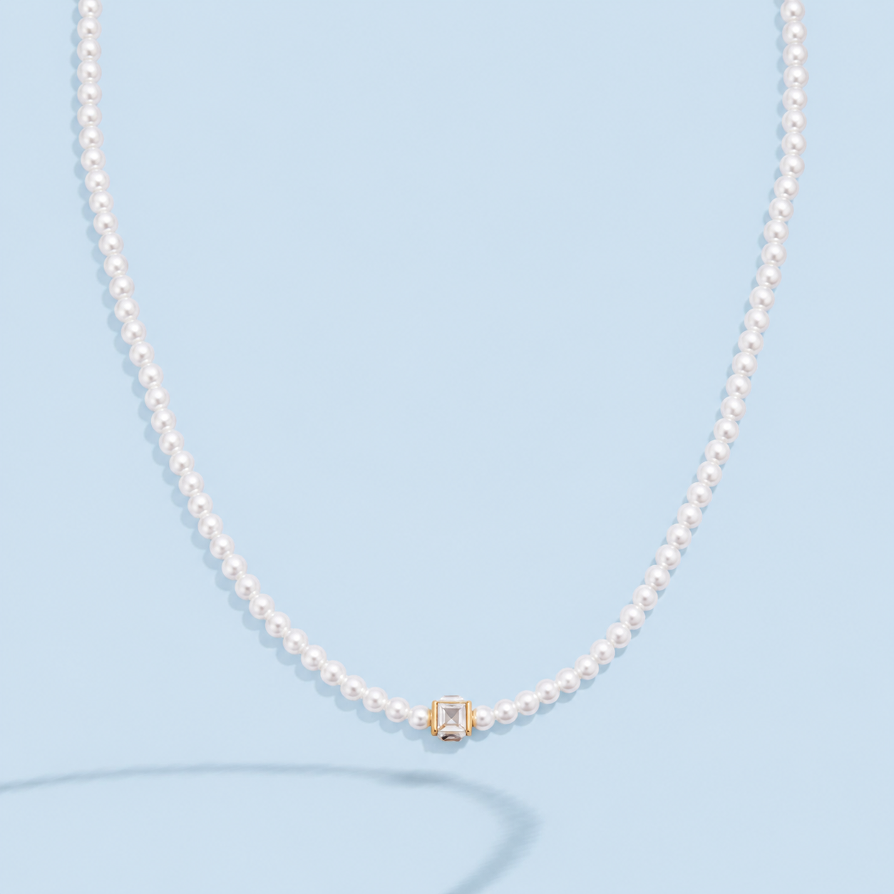 Marissa faux pearl necklace with a clear square crystal in a gold-tone setting on a pale blue background.