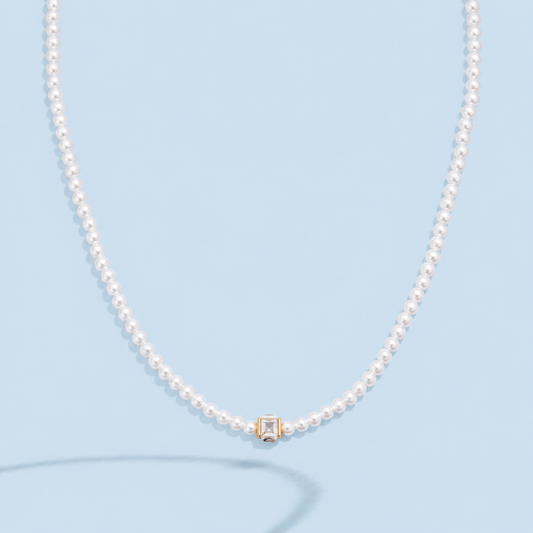 Marissa faux pearl necklace with a clear square crystal in a gold-tone setting on a pale blue background.