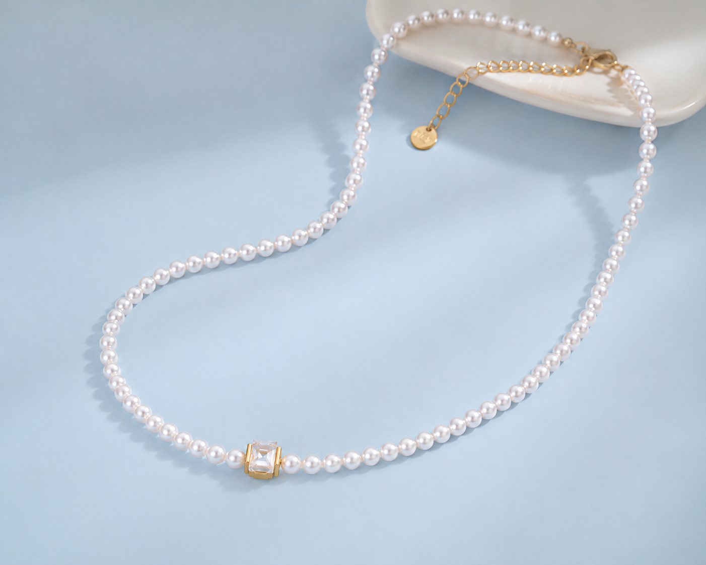 Marissa faux pearl necklace with a clear square crystal and gold-tone details styled on a pale blue background.