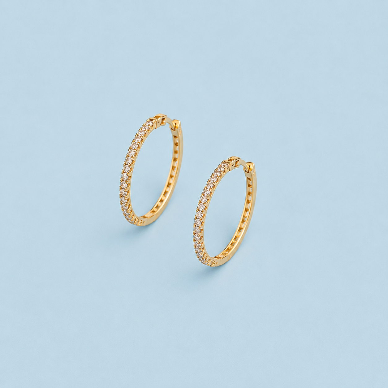 Monroe gold pavé hoop earrings with clear stones displayed on a light blue background.