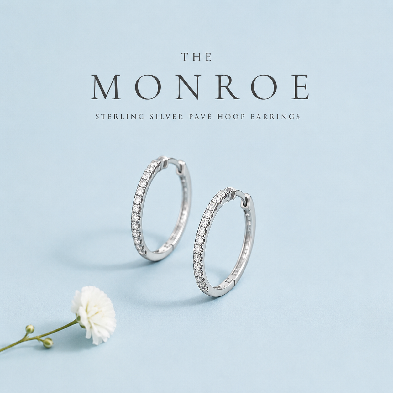  Monroe sterling silver pavé hoop earrings with clear stones displayed on a light blue background.