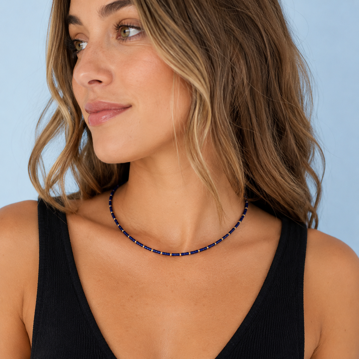 Model wearing the Navy Lapis Necklace with genuine lapis lazuli beads and 18K gold-plated details against a light blue background.