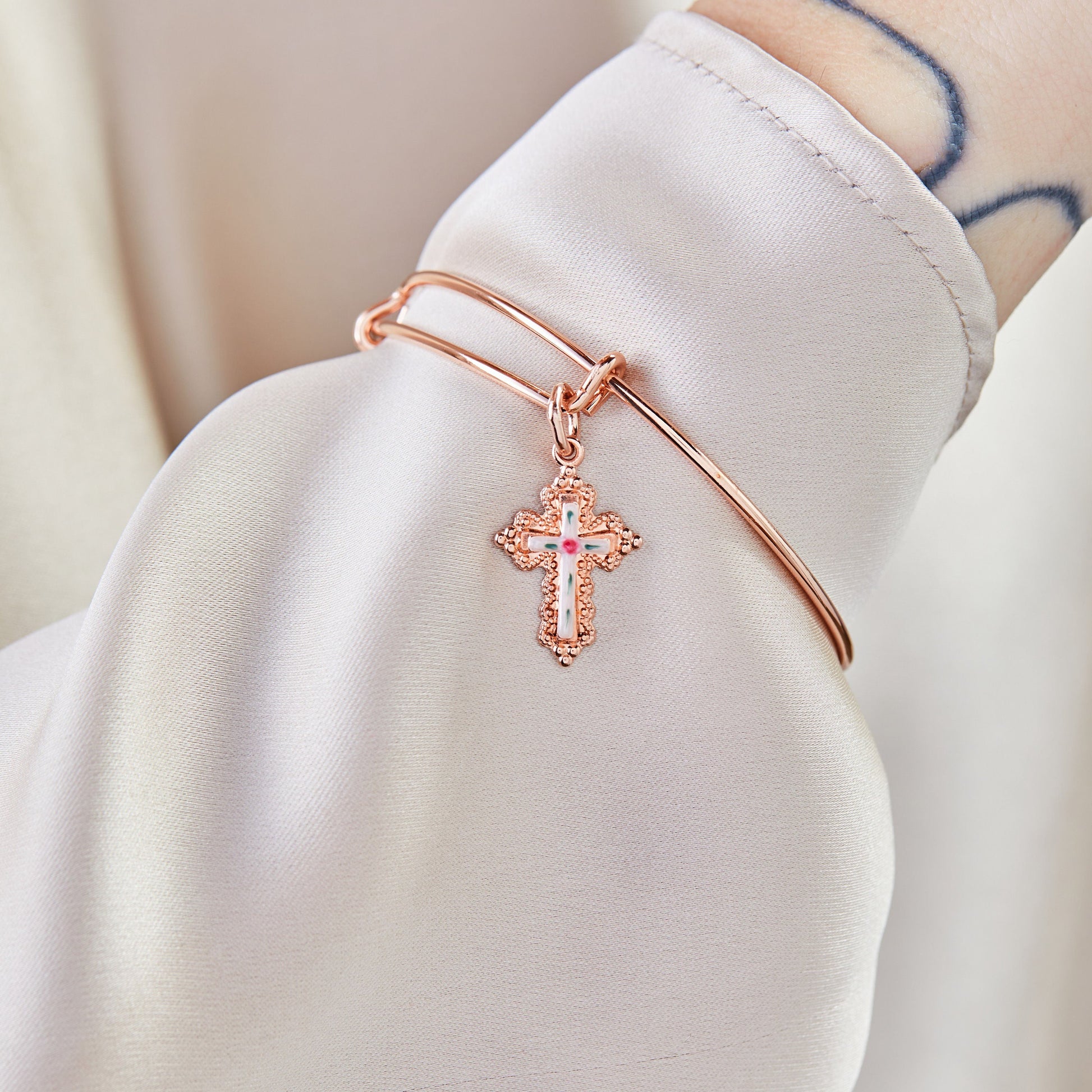     Paisley rose gold floral cross charm bangle bracelet worn on the wrist.