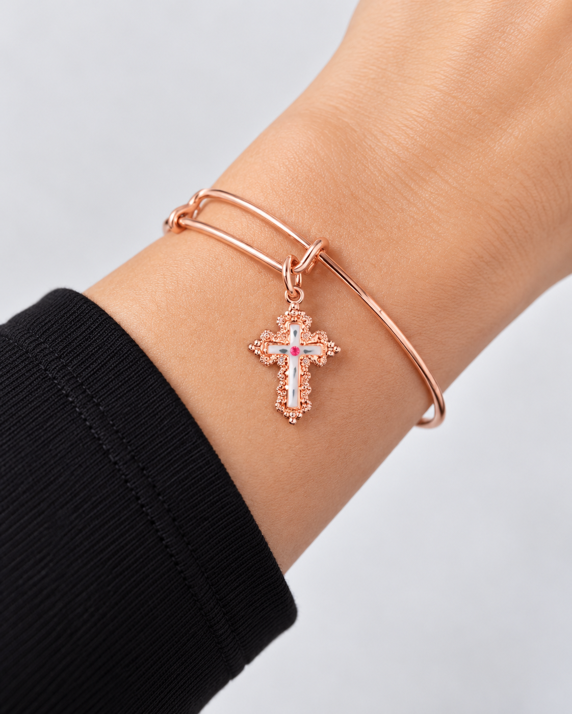 Close-up of the Paisley rose gold-tone bangle bracelet with a cross charm worn on the wrist with a black sleeve.