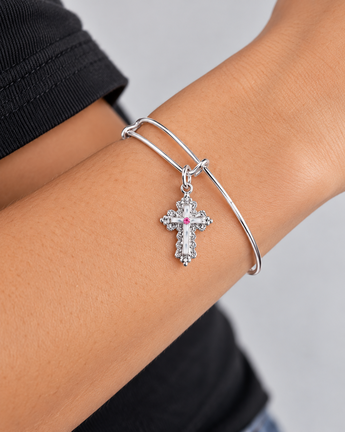 Close-up of the Paisley silver-tone bangle bracelet with a cross charm worn on the wrist with a black sleeve.