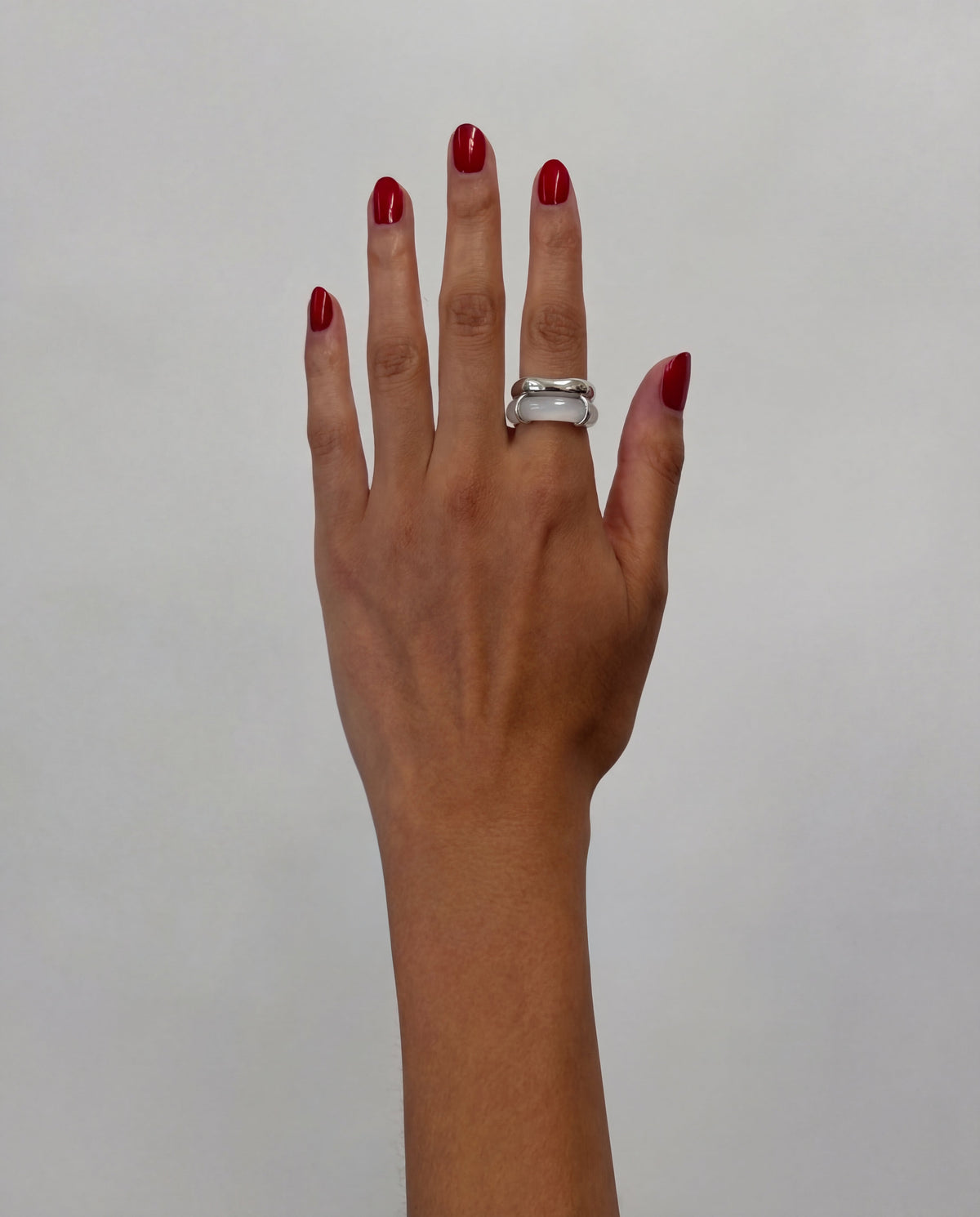 Hand with burgundy-red nail polish wearing the Rhodes white chalcedony ring with a chunky silver-tone setting.