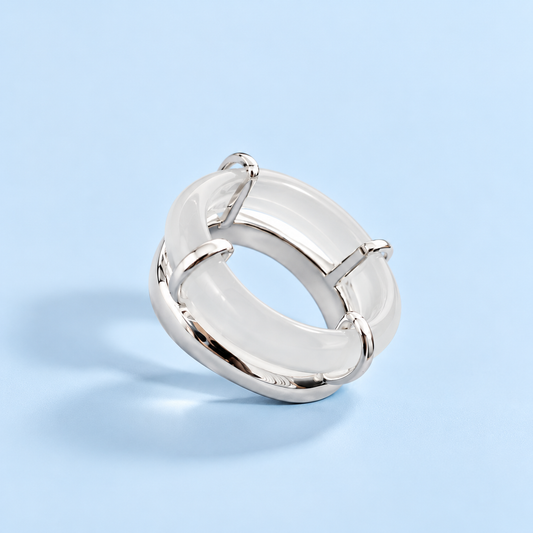 Rhodes White Chalcedony Sculptural Ring featuring a polished silver-plated brass setting and curved white chalcedony stone, photographed against The Riann Ashlyn Collection's signature pale blue background.