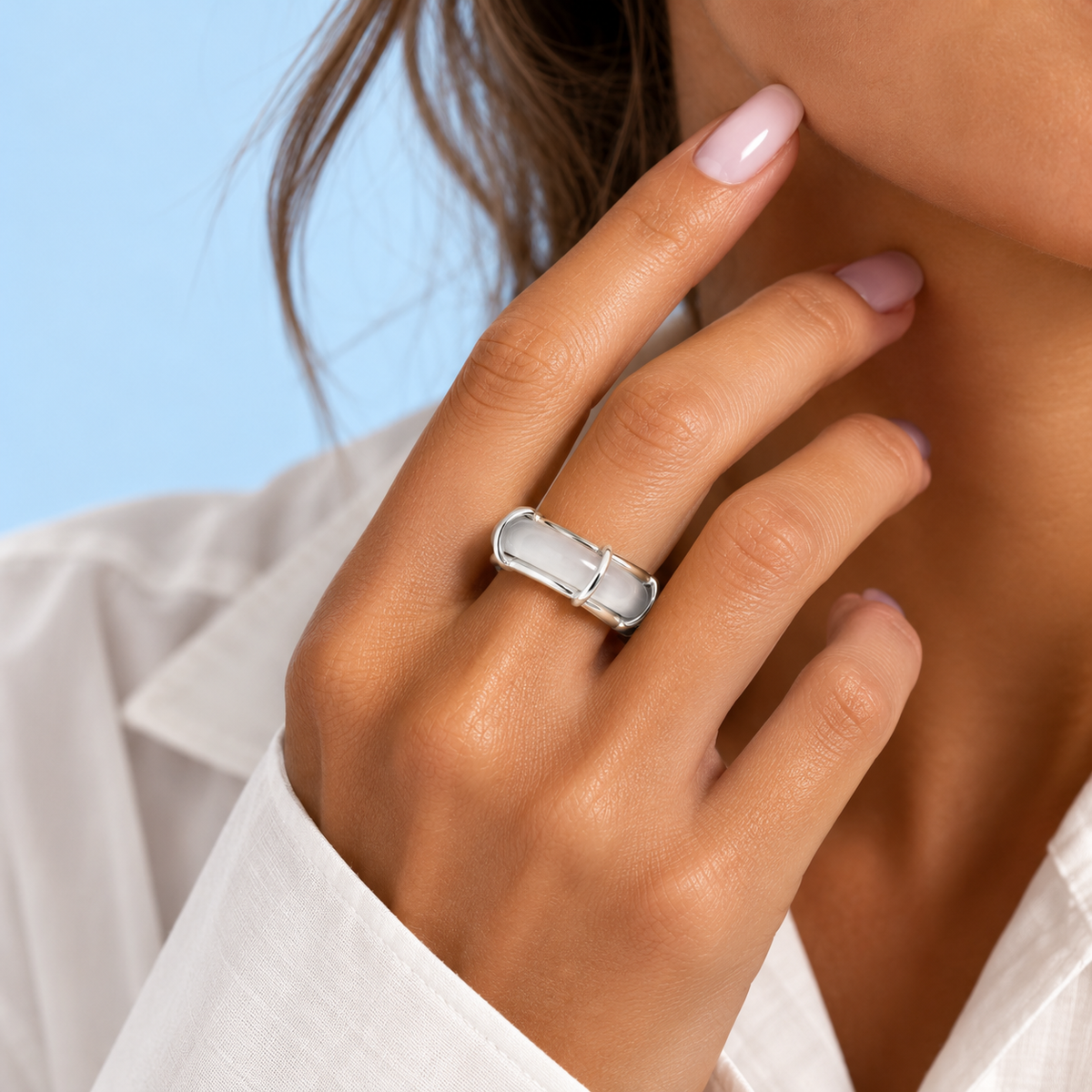Model wearing the Rhodes White Chalcedony Sculptural Ring from The Riann Ashlyn Collection, featuring a polished silver-plated brass setting, styled with a white button-down shirt against a soft RA blue background.