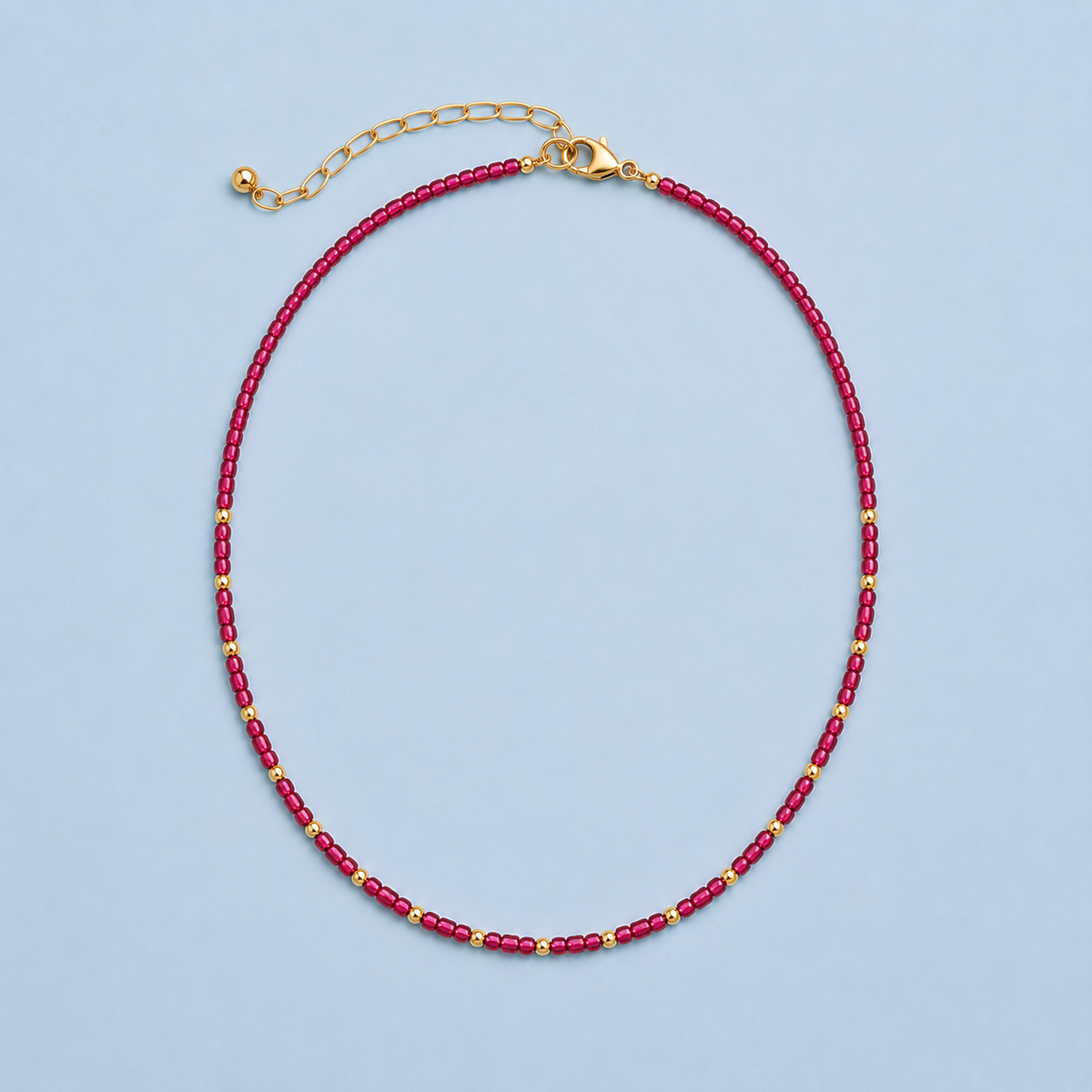 Rory Ruby Necklace with ruby-toned beads and 18K gold-plated details on a light blue background.