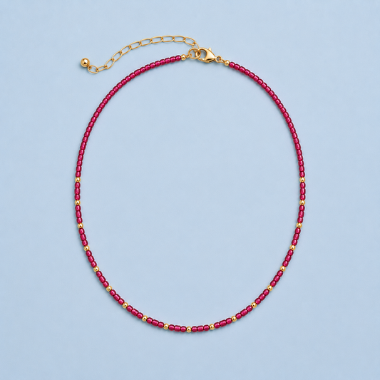 Rory Ruby Necklace with ruby-toned beads and 18K gold-plated details on a light blue background.