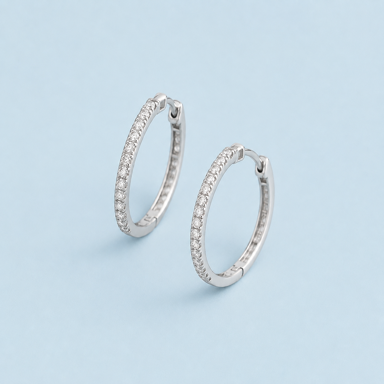 Silver hoop earrings with pavé-set clear stones on a light blue background.